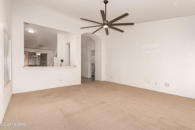 unfurnished living room featuring arched walkways, carpet, and ceiling fan