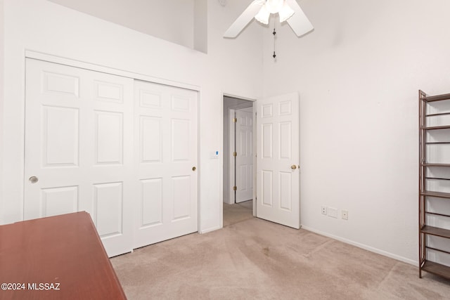 unfurnished bedroom with a high ceiling, ceiling fan, light colored carpet, and a closet