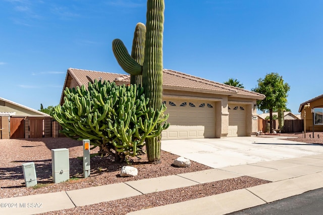 view of front facade with fence, a tiled roof, a garage, concrete driveway, and stucco siding