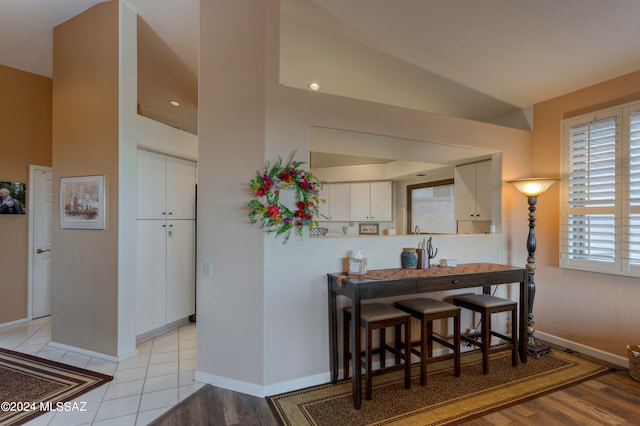 kitchen with white cabinetry, kitchen peninsula, light wood-type flooring, lofted ceiling, and a kitchen bar