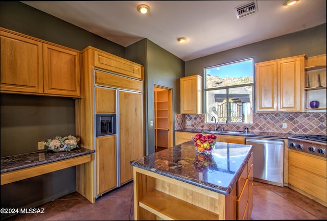 kitchen with sink, a kitchen island, backsplash, stainless steel appliances, and dark stone counters