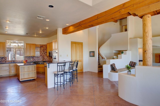 kitchen with tasteful backsplash, visible vents, dark countertops, a breakfast bar, and light brown cabinets