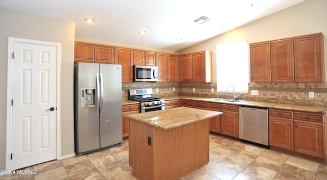 kitchen with a kitchen island, light stone countertops, stainless steel appliances, sink, and vaulted ceiling