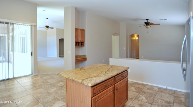 kitchen featuring light stone countertops, stainless steel refrigerator, a kitchen island, and ceiling fan