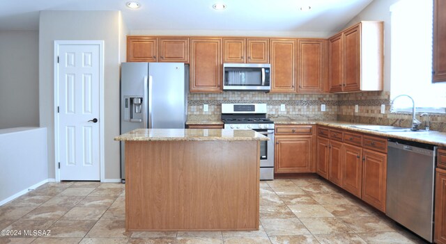 kitchen with light stone counters, sink, backsplash, stainless steel appliances, and a center island