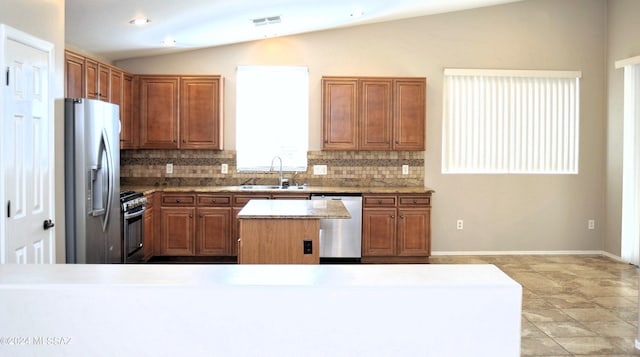 kitchen with lofted ceiling, sink, backsplash, stainless steel appliances, and a center island