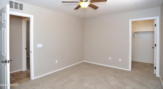 unfurnished bedroom featuring light carpet, a spacious closet, ceiling fan, and a closet