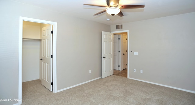 unfurnished bedroom with a walk in closet, ceiling fan, a closet, and light colored carpet