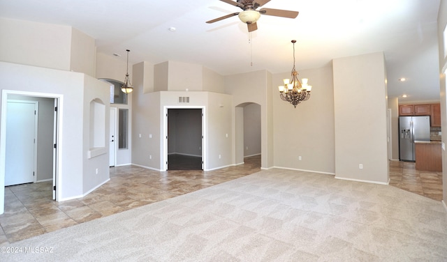 unfurnished living room featuring a high ceiling, ceiling fan with notable chandelier, and light colored carpet