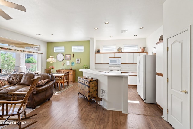 kitchen with open floor plan, white appliances, light countertops, a breakfast bar area, and hardwood / wood-style floors