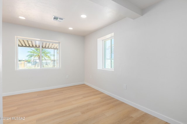 unfurnished room with light hardwood / wood-style flooring and beamed ceiling