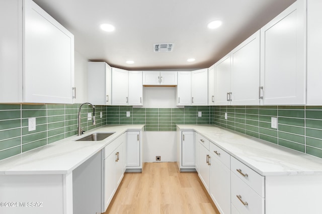 kitchen with white cabinetry, backsplash, light stone countertops, light wood-type flooring, and sink