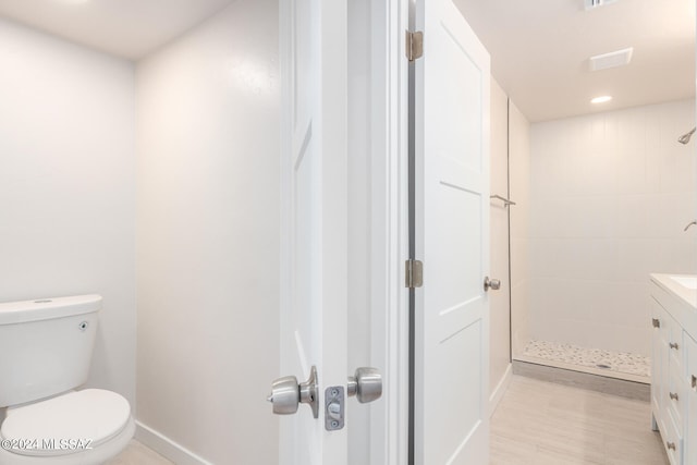 bathroom with a tile shower, vanity, and toilet