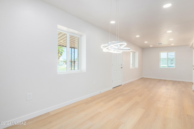 spare room featuring light wood-type flooring, a chandelier, and a wealth of natural light