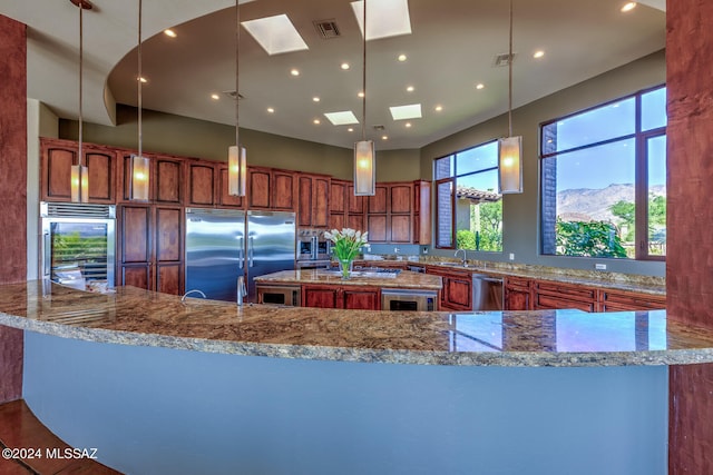 kitchen with a large island, stainless steel appliances, sink, a skylight, and decorative light fixtures