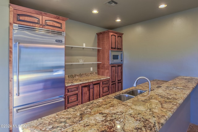 kitchen with built in appliances, light stone counters, and sink