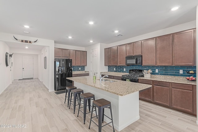 kitchen with sink, a breakfast bar, a kitchen island with sink, light stone counters, and black appliances