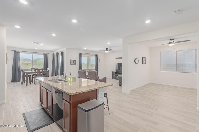 kitchen featuring sink, light hardwood / wood-style floors, light stone countertops, a center island with sink, and stainless steel dishwasher