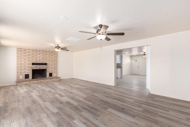 unfurnished living room with wood-type flooring, ceiling fan, and a brick fireplace