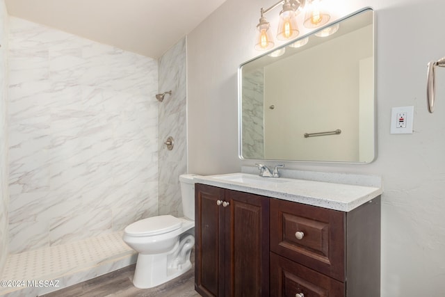 bathroom with a tile shower, wood-type flooring, vanity, and toilet