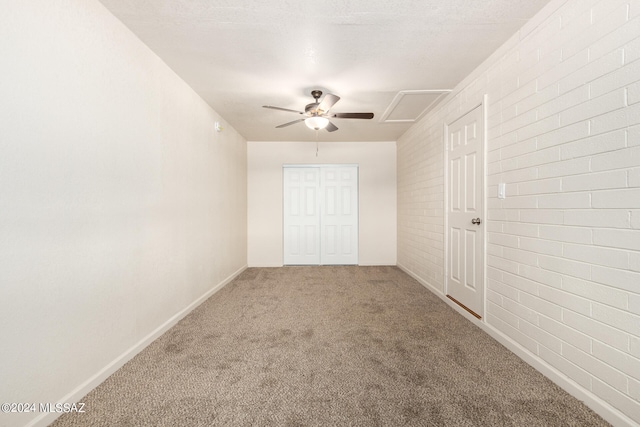 spare room featuring a textured ceiling, carpet flooring, ceiling fan, and brick wall