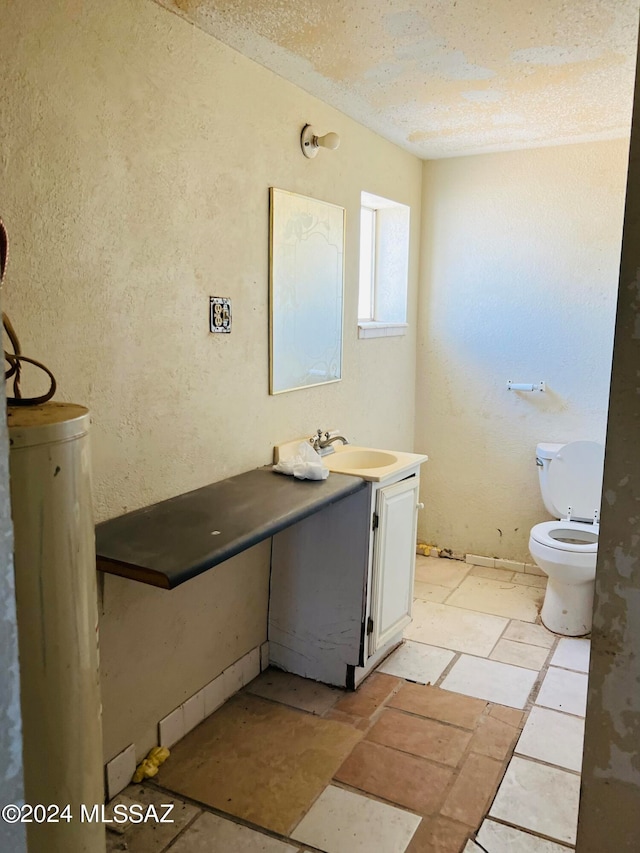 bathroom with water heater, a textured ceiling, vanity, and toilet