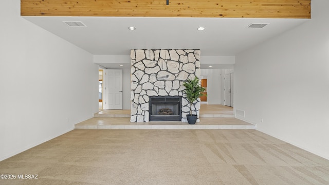 unfurnished living room featuring beamed ceiling, a stone fireplace, and light colored carpet