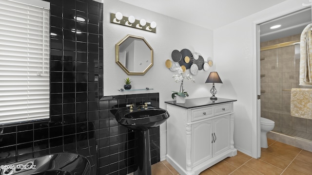 bathroom featuring tile patterned flooring, a tile shower, toilet, and sink