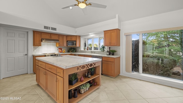 kitchen featuring tile counters, stainless steel appliances, an island with sink, decorative backsplash, and light tile patterned floors