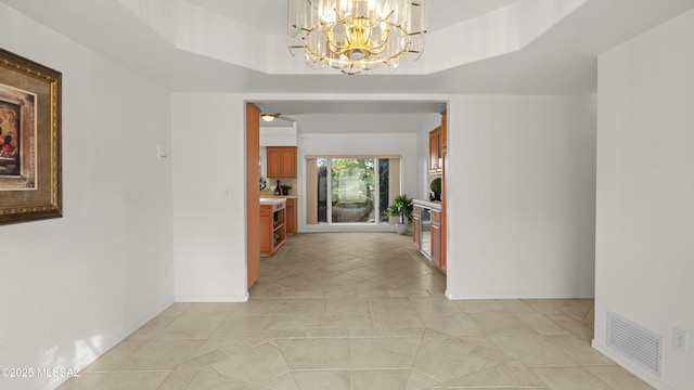 hall featuring a raised ceiling, light tile patterned flooring, and an inviting chandelier