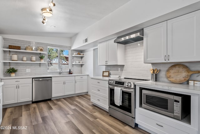 kitchen featuring decorative backsplash, wall chimney exhaust hood, stainless steel appliances, vaulted ceiling, and white cabinetry