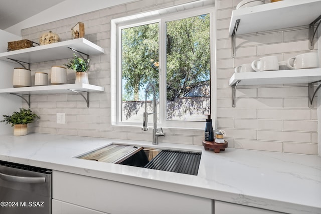 kitchen with backsplash, sink, stainless steel dishwasher, white cabinetry, and light stone counters