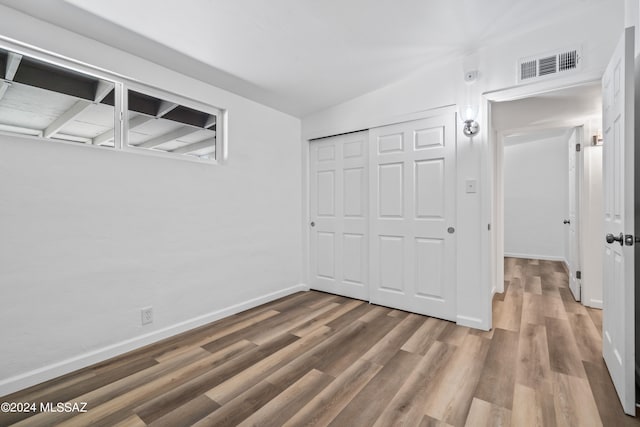 unfurnished bedroom with a closet, hardwood / wood-style flooring, and vaulted ceiling