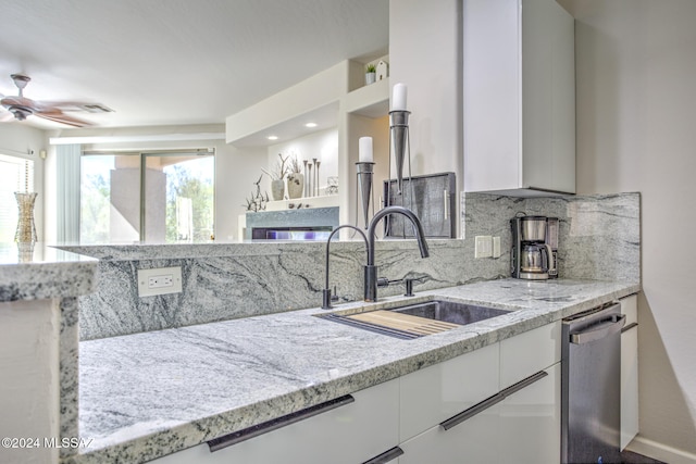 kitchen featuring stainless steel dishwasher, sink, light stone countertops, and white cabinets