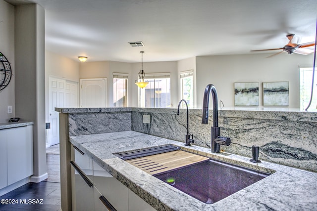 kitchen with light stone counters, pendant lighting, sink, dark wood-type flooring, and ceiling fan