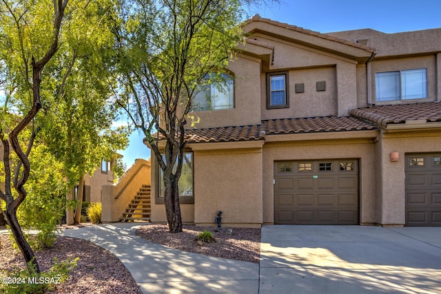 multi unit property with a garage, stucco siding, a tiled roof, concrete driveway, and stairway