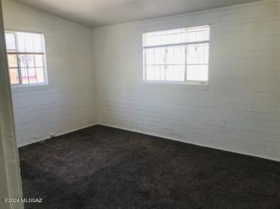 carpeted empty room featuring vaulted ceiling and brick wall