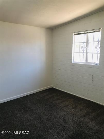 spare room featuring dark carpet, baseboards, and brick wall