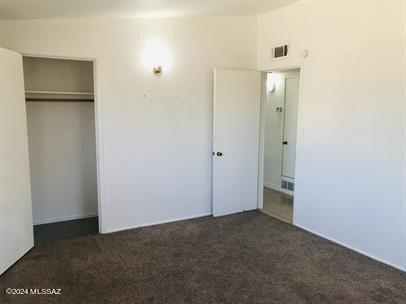 unfurnished bedroom with dark carpet and a closet