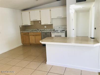 kitchen with white electric range, light tile patterned flooring, lofted ceiling, and visible vents