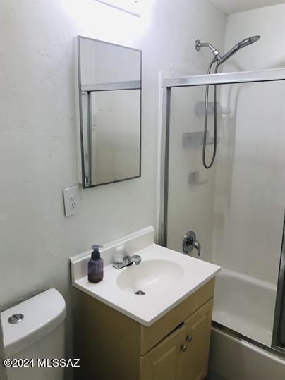 full bathroom with enclosed tub / shower combo, vanity, and toilet