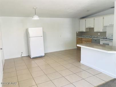 kitchen with vaulted ceiling, white appliances, light countertops, white cabinets, and pendant lighting