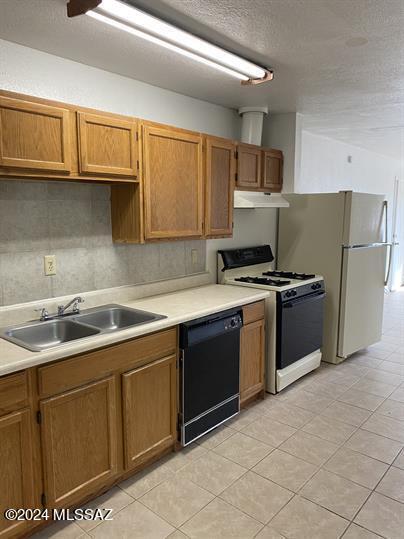 kitchen featuring white appliances, light countertops, a textured ceiling, under cabinet range hood, and a sink
