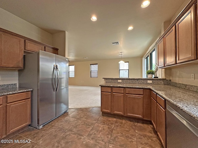 kitchen with stainless steel appliances, dark carpet, hanging light fixtures, and dark stone counters