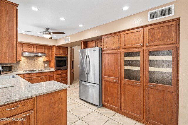 kitchen with sink, decorative backsplash, appliances with stainless steel finishes, light stone countertops, and ceiling fan