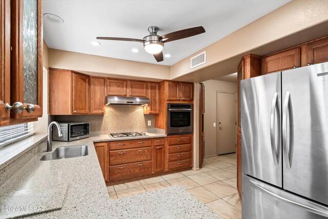 kitchen featuring sink, decorative backsplash, appliances with stainless steel finishes, light stone countertops, and ceiling fan