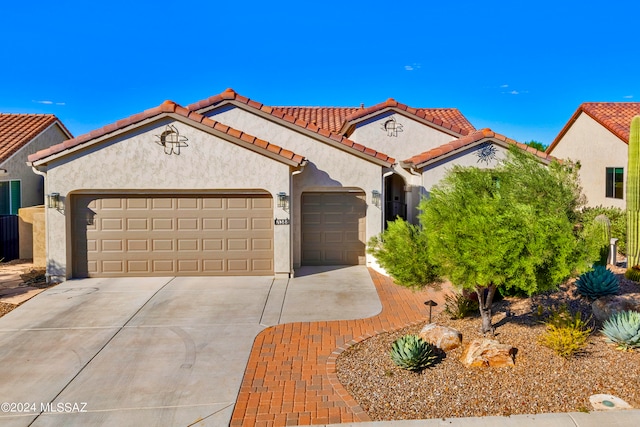 mediterranean / spanish-style home featuring driveway, a tiled roof, an attached garage, and stucco siding