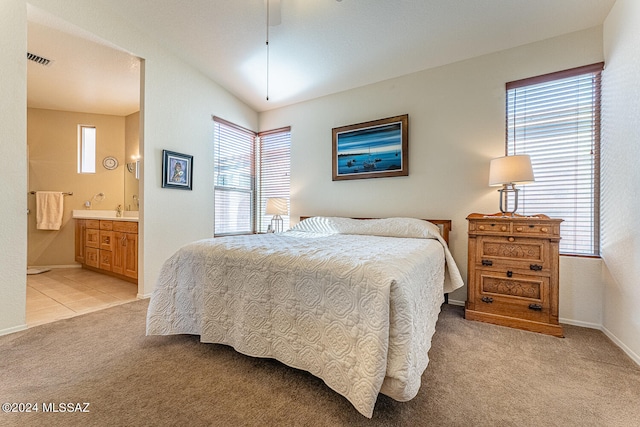 bedroom with multiple windows, connected bathroom, and light colored carpet