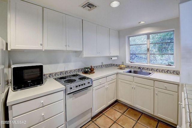 kitchen with white cabinetry, sink, light tile patterned floors, and range