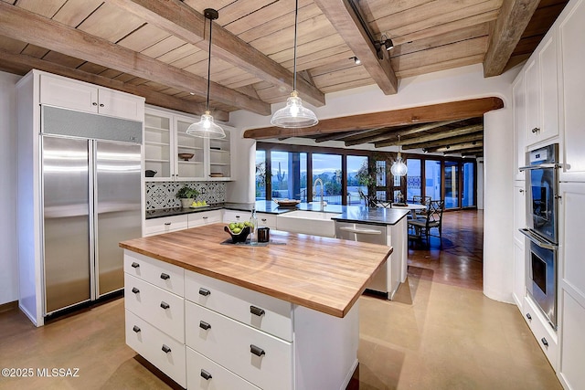 kitchen featuring stainless steel appliances, beam ceiling, a center island, white cabinetry, and butcher block counters